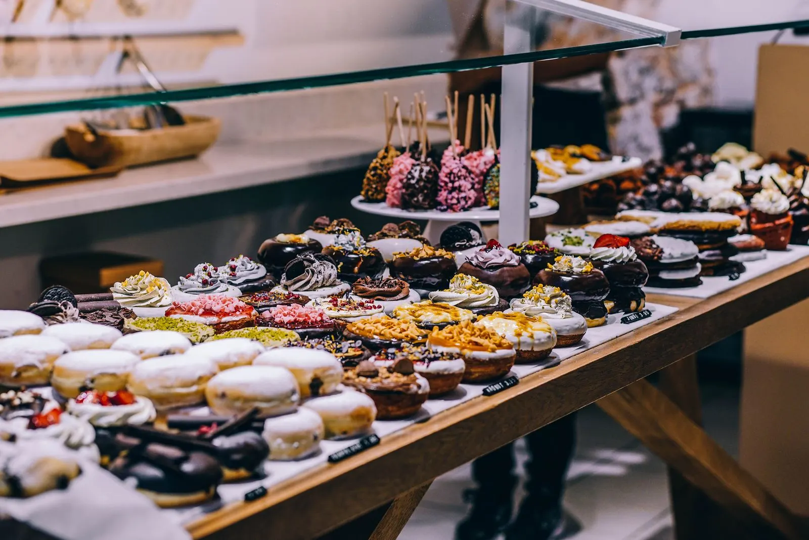 A bakery counter lined with glossy chocolate-topped pastries, cream-filled donuts, and berry tarts