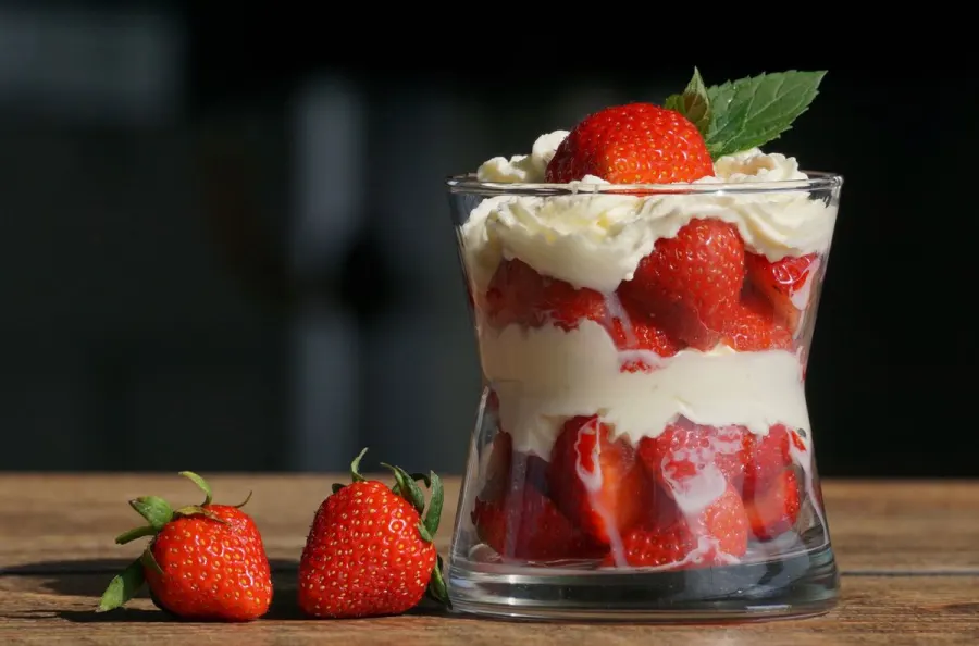 A layered strawberry cream parfait in a glass, garnished with fresh mint and whole strawberries
